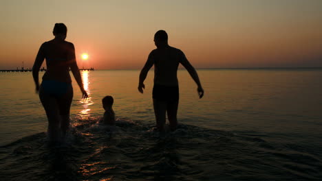 Eltern-Spielen-Mit-Ihrem-Sohn-Bei-Sonnenuntergang-Ball-Im-Meer