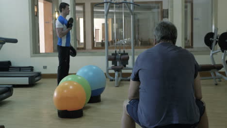 Man-exercising-with-weight-disks-his-friend-having-a-rest