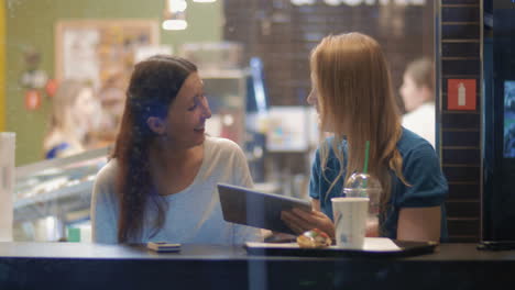 Female-friends-talking-and-using-touch-pad-in-cafe