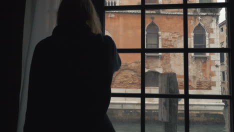 Woman-opening-window-and-enjoying-Venice-scenes