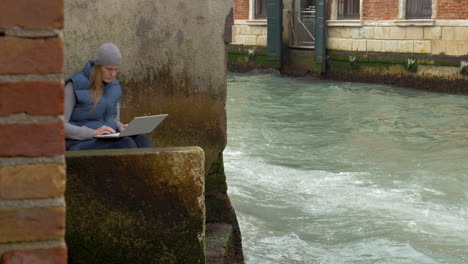 Woman-using-laptop-by-the-canal-with-sailing-boat