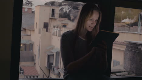 Woman-using-tablet-PC-sitting-on-windowsill