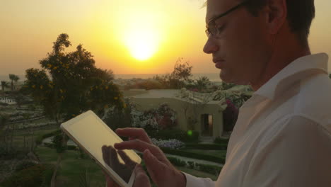 Businessman-on-vacation-using-touch-pad-at-sunset