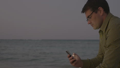 Young-man-using-smart-phone-by-sea-in-the-evening