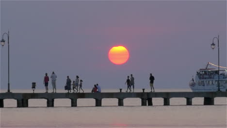 Ferry-Navegando-Por-El-Muelle-Con-Gente-Al-Atardecer