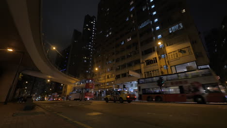 Vista-De-La-Ciudad-Nocturna-Y-El-Edificio-Más-Alto-Con-Una-Calle-Muy-Transitada-Por-La-Que-Pasan-Autobuses-Y-Automóviles-De-Dos-Pisos.