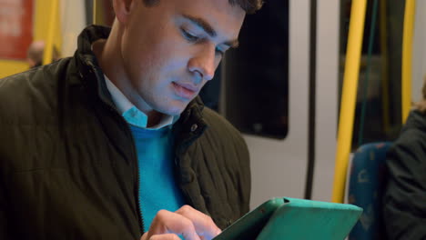 Male-passenger-with-touch-pad-in-subway-train