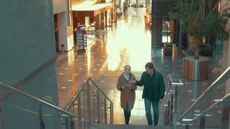 Young-couple-with-pad-going-upstairs-in-modern-trade-centre