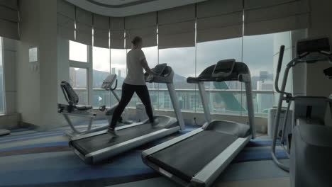 Clip-De-Mujer-En-La-Cinta-De-Correr-En-El-Gimnasio-Mirando-La-Ventana-Con-El-Paisaje-Urbano-De-Hong-Kong,-China