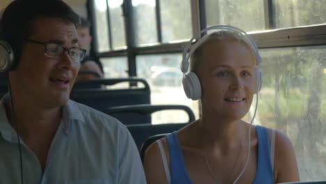 Young-couple-listening-to-music-on-headphones-during-the-bus-ride-they-dance-to-the-music-man-singing