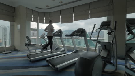 Clip-Einer-Frau-Auf-Dem-Laufband-Im-Fitnesscenter,-Die-Auf-Ein-Fenster-Mit-Stadtbild-Von-Hongkong,-China-Blickt