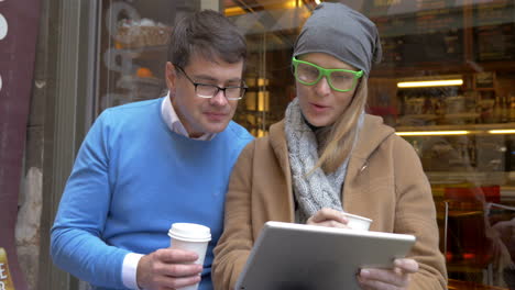 Young-couple-having-coffee-and-using-pad-in-city