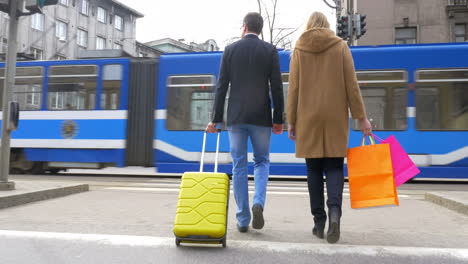 Pareja-Con-Maleta-Y-Bolsas-De-Compras-Cruzando-La-Calle