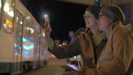 Friends-making-selfie-and-using-pad-at-tram-stop