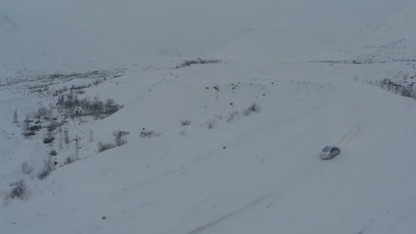 Car-on-heavy-snowy-road-in-mountains-aerial-view