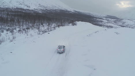 Aerial-view-of-car-driving-on-snowy-mountain-road