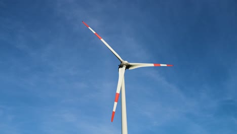 Low-angle-shot-of-wind-turbines-working-and-generating-green-electric-energy-in-a-wind-farm-under-blue-sky-on-a-sunny-day