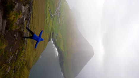 Hombre-Vestido-Con-Chaqueta-Azul-Balanceándose-Sobre-Una-Roca-En-Vidoy,-Islas-Feroe