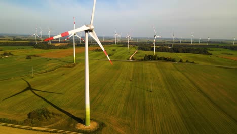Drone-shot-of-the-wind-turbines-working-in-a-wind-farm-generating-green-electric-energy-on-a-wide-green-field-on-a-sunny-day,-use-of-renewable-resources-of-energy,-slide-right