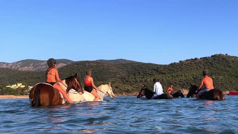 Tourists-enjoying-refreshing-horseback-ride-in-the-tranquil-sea-water-of-Corsica-island-in-France