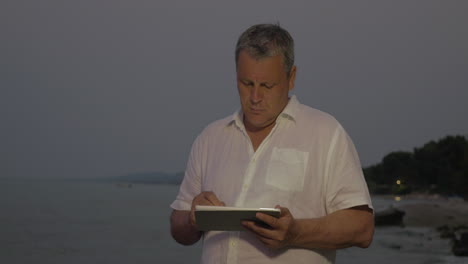 Man-typing-on-tablet-while-standing-on-beach