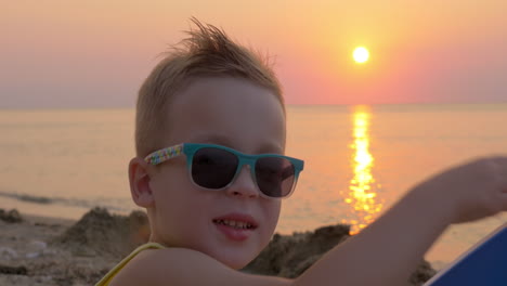 Süßer-Junge-Mit-Sonnenbrille-Am-Strand-Bei-Sonnenuntergang