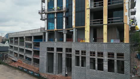 Rising-drone-shot-showing-modern-building-with-parking-area-at-Building-phase---worker-installing-windows-in-Atlanta