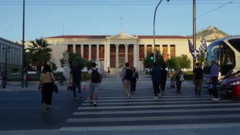 Pedestrians-cross-at-a-busy-intersection-in-Athens-with-the-University-in-the-backdrop-during-golden-hour