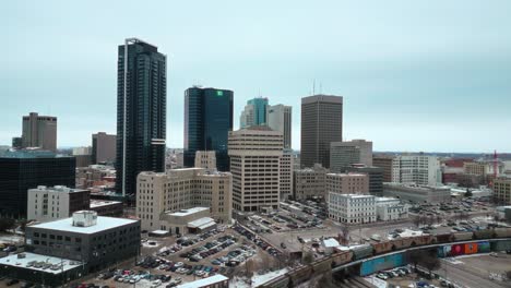 Establishing-Orbit-Winnipeg-Manitoba-Canada-Downtown-Skyscraper-Buildings-in-City-Overcast-Blue-Sky-Landscape-Skyline-Snowing-Winter-Drone-4k-Shot-with-Multicolored-Train-Passing-Through