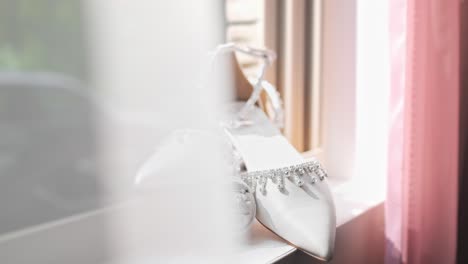 A-beautiful-shot-of-wedding-shoes-laying-on-the-window-sill-with-rings-at-the-base-of-the-shoes