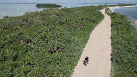 Motorcyclist-travels-alone-through-sunny-island-sea-beach-Biosphere-Tulum-Aerial-Drone-Shot
