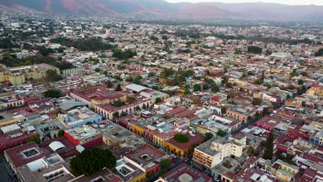 An-aerial-drone-shot-of-Oaxaca-City,-Mexico,-showing-colourful-buildings-and-a-mountainous-landscape-in-the-distance