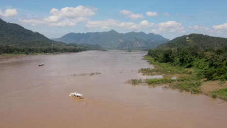 Vuelo-Aéreo-Sobre-El-Río-Mekong-En-Un-Día-Soleado-Con-Un-Barco-Fluvial-Visto-Cruzándolo-En-Luang-Prabang