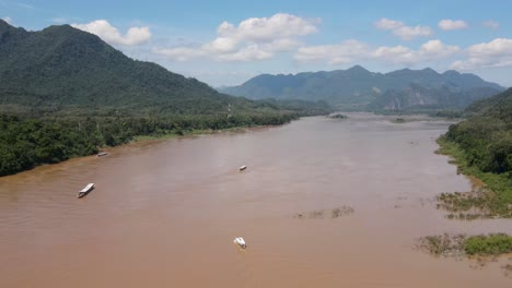 Vuelo-Aéreo-Sobre-El-Poderoso-Río-Mekong-En-Un-Día-Soleado-Con-Barcos-Fluviales-Vistos-Cruzándolo-En-Luang-Prabang