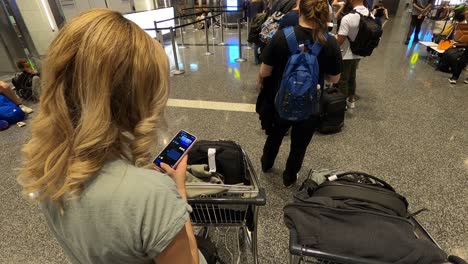 Una-Chica-En-El-Aeropuerto-Hablando-Por-Teléfono,-Esperando-En-La-Cola-Para-Facturar-El-Equipaje.