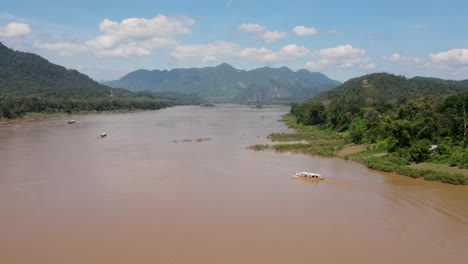 Vuelo-Aéreo-Sobre-El-Poderoso-Río-Mekong-En-Un-Día-Soleado-Con-Un-Barco-Fluvial-Visto-Cruzándolo-En-Luang-Prabang