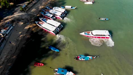 Descending-pedestal-aerial-drone-shot-of-Rawai-beachfront-with-its-array-of-speedboats,-longtail-boats,-and-fishing-boats-anchored-in-front-of-the-busy-coastline,-in-Phuket,-Thailand