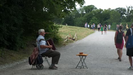 Older-gentleman-playing-his-accordion-entertaining-visitors,-local-park