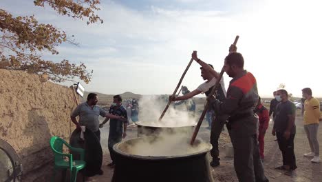 Group-cooking-party-outside-in-nature-outdoor-Persian-gathering-to-cook-ash-the-Persian-stew-in-Iran-Yazd-Ardakan-public-ceremony-new-year-meat-in-big-pot-on-fire-wood-bonfire-campfire-coal-hot-flame