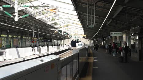 N700-Shinkansen-bullet-train-arriving-at-Shin-Kobe-station-platform-with-people-waiting-to-board,-Japan
