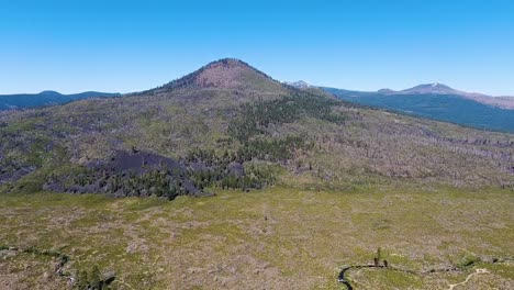 Aerial-footage-of-a-beautiful-hill-covered-by-lush-greenery-and-pine-trees,-under-a-blue-sky-in-Lassen-National-Forest