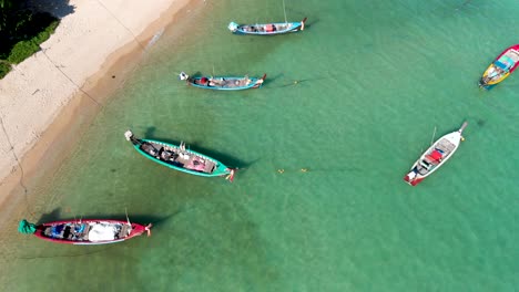 Aerial-drone-shot-fly-over-and-slowly-doing-a-descending-pedestal-of-Rawai-Beach,-showing-the-wooden-long-tail-boats,-white-sandy-beach-and-crystal-clear-waters-of-Rawai-beach-in-Phuket,-Thailand