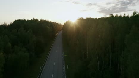 Revealing-drone-shot-of-road-with-car-going-through-spruce-forest-during-sunset