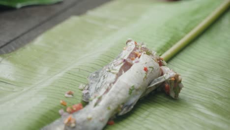Closeup-of-fresh-fish-wrapped-in-Banana-leaves-filled-with-fresh-herbs-getting-prepared-for-lunch