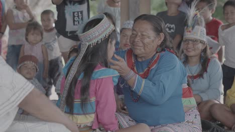 An-older-indigenous-woman-is-holding-the-face-of-a-young-girl-surrounded-by-their-community,-Peru