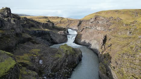 Una-Cascada-Escondida-Detrás-De-Algunas-Montañas-En-El-Sur-De-Islandia-Durante-El-Otoño,-Aérea