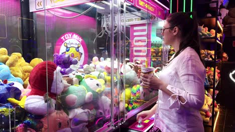 Woman-with-glasses-plays-with-a-claw-crane-to-win-stuffed-animals-of-popular-childrens-characters