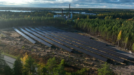 Aerial-view-around-sunlight-collector-field-in-middle-of-autumn-forest-and-industrial-chimney