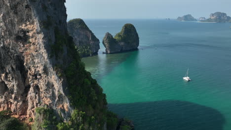 Aerial-views-around-cliff-overlooking-Ko-Rang-Nok-Island-with-a-sailing-boat-in-Railay,-Thailand
