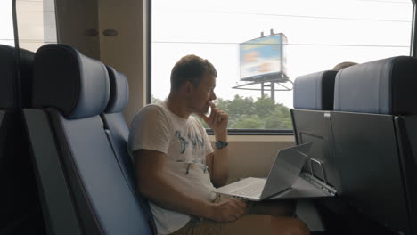 Blick-Auf-Einen-Jungen-Mann,-Der-Im-Zug-Fährt-Und-Mit-Einem-Laptop-Auf-Dem-Tisch-Vor-Dem-Fenster-Arbeitet,-Niederlande